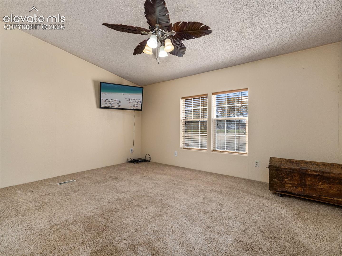 Textured ceiling, wall-to-wall carpeting, ceiling fan with light fixture, and dual windows with blinds