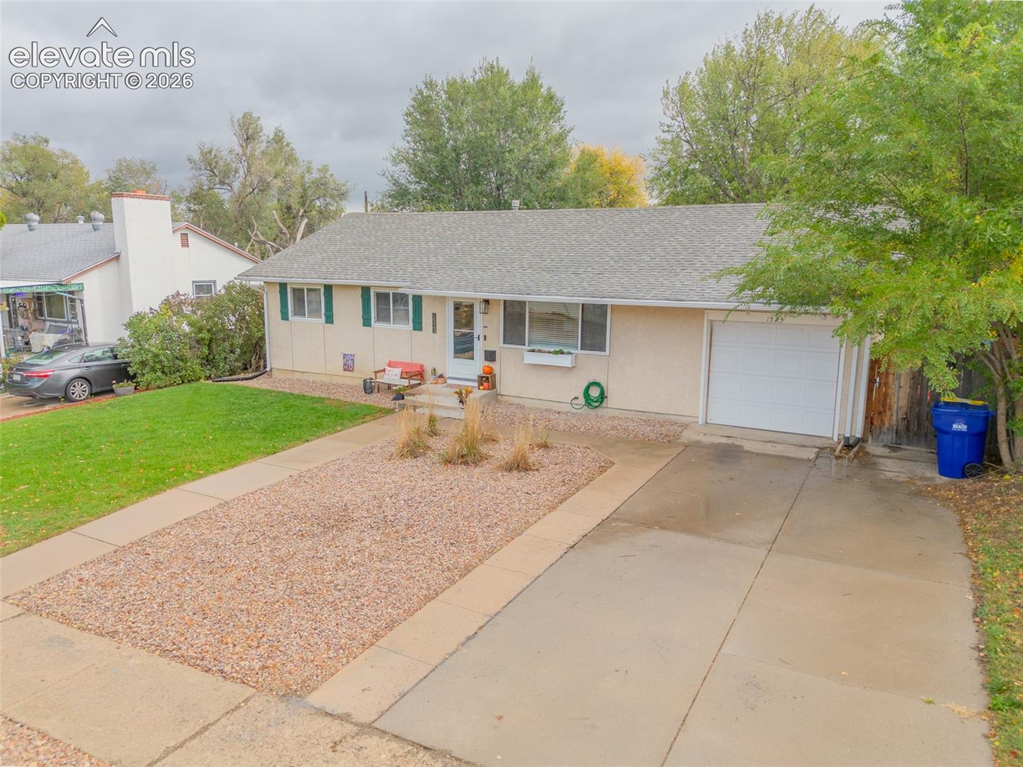 Single-story exterior featuring light-toned siding, a concrete driveway, an attached garage, and a gravel front yard