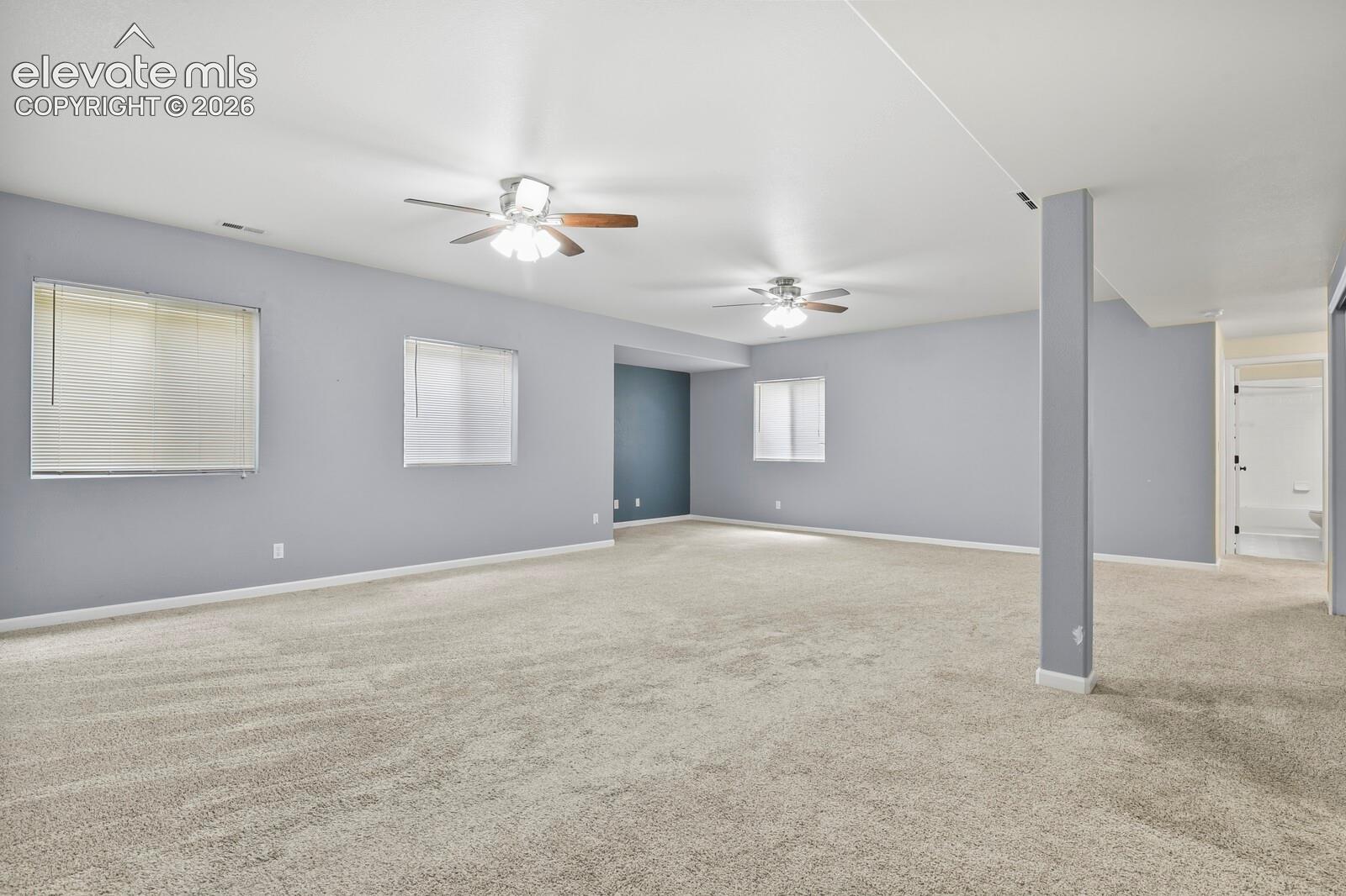 Spacious room with light gray walls, plush carpeting, multiple ceiling fans, and natural light from windows