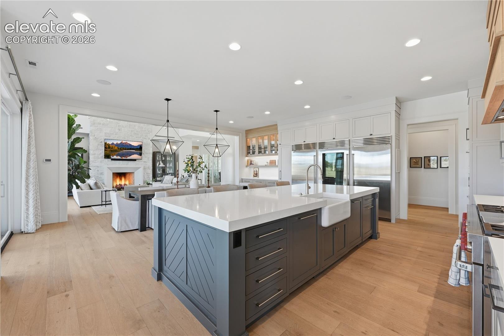 Kitchen featuring a large central island with quartz countertops, custom cabinetry, a farmhouse-style sink, and light-toned wood-finish flooring