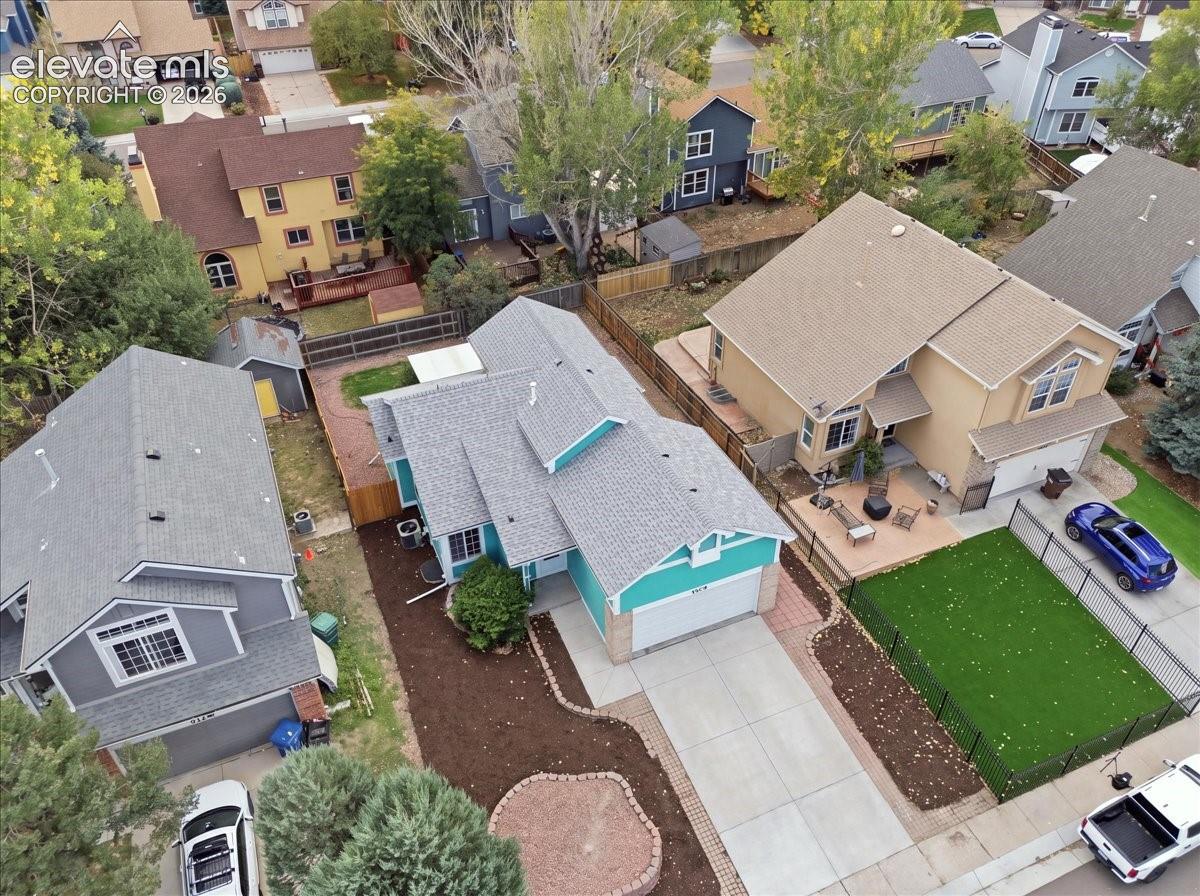 Aerial perspective of residential property featuring a multi-gabled shingle roof, attached two-car garage, concrete driveway, and established tree canopy