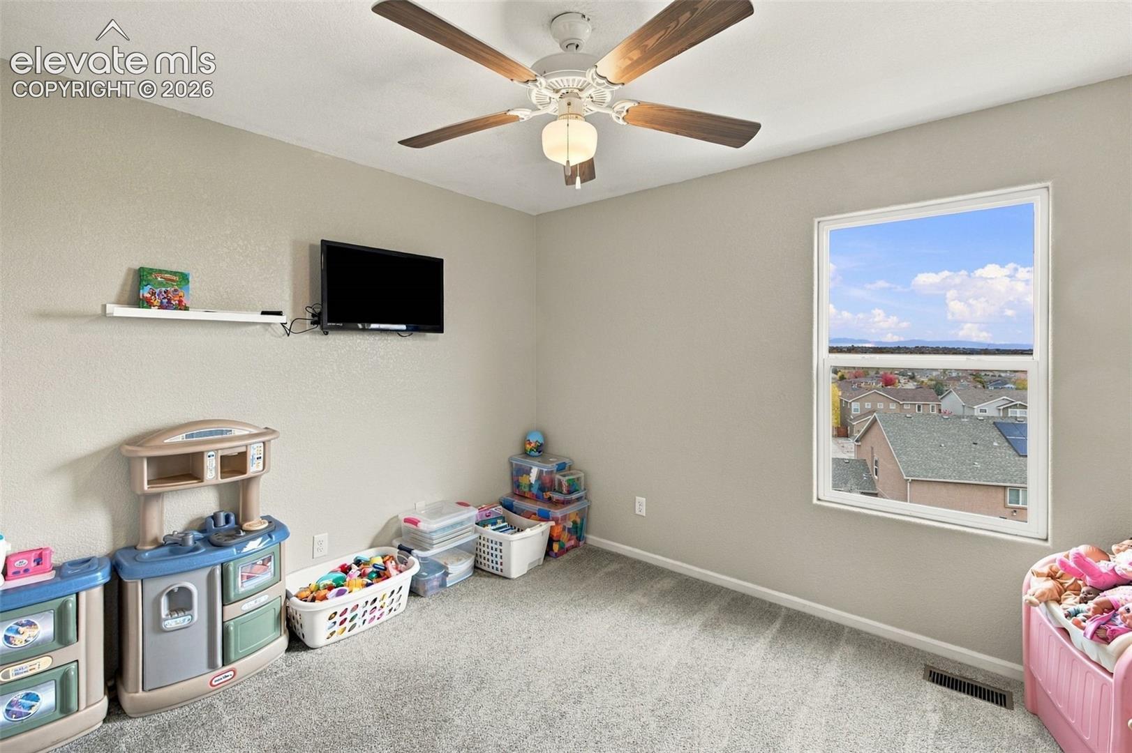 Neutral-toned room featuring plush carpeting, a single-hung window with a horizon backdrop, and a ceiling fan with integrated lighting