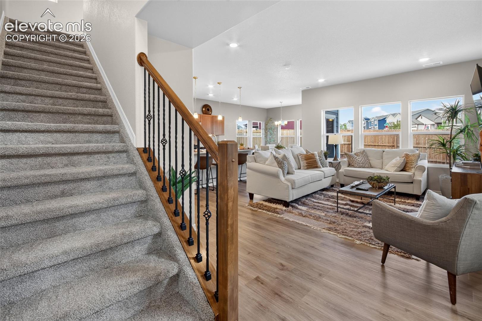 Carpeted staircase featuring a wooden handrail and black metal balusters, complemented by wood-finish flooring, recessed lighting, and large windows