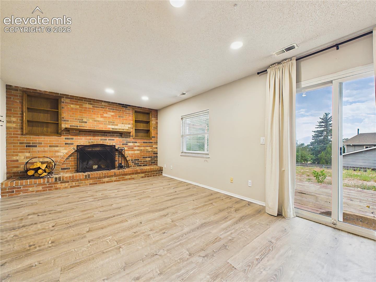 Bright lower-level family room featuring a striking brick fireplace and sliding glass door providing easy access to the backyard deck.