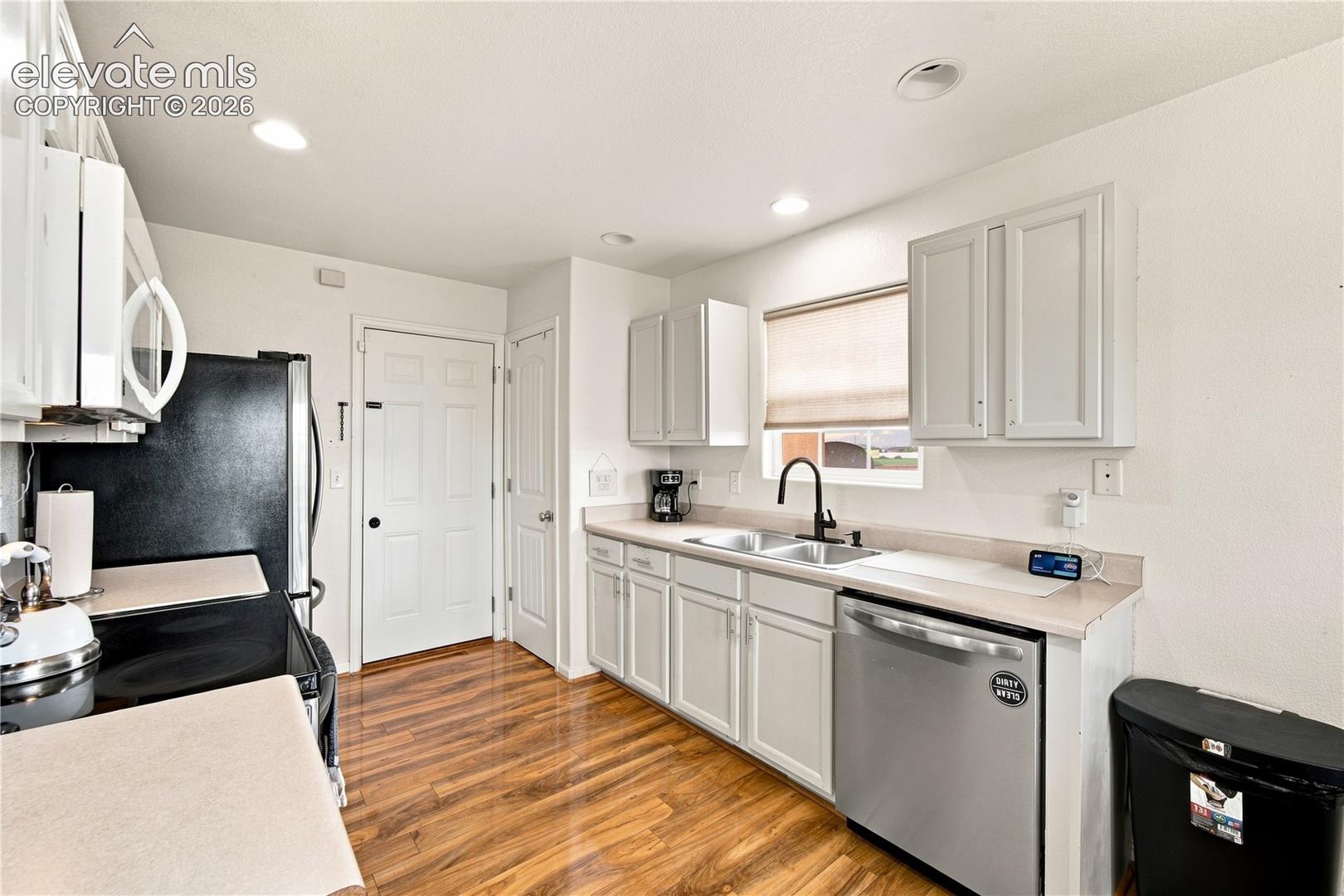 Kitchen featuring wood-finish flooring, white cabinetry, light-toned countertops, a dual-basin sink with a matte black faucet, and recessed lighting
