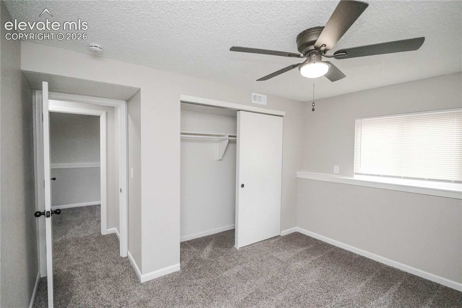 Neutral-toned room featuring textured ceilings, carpeted flooring, a ceiling fan with integrated lighting, and a closet with sliding doors