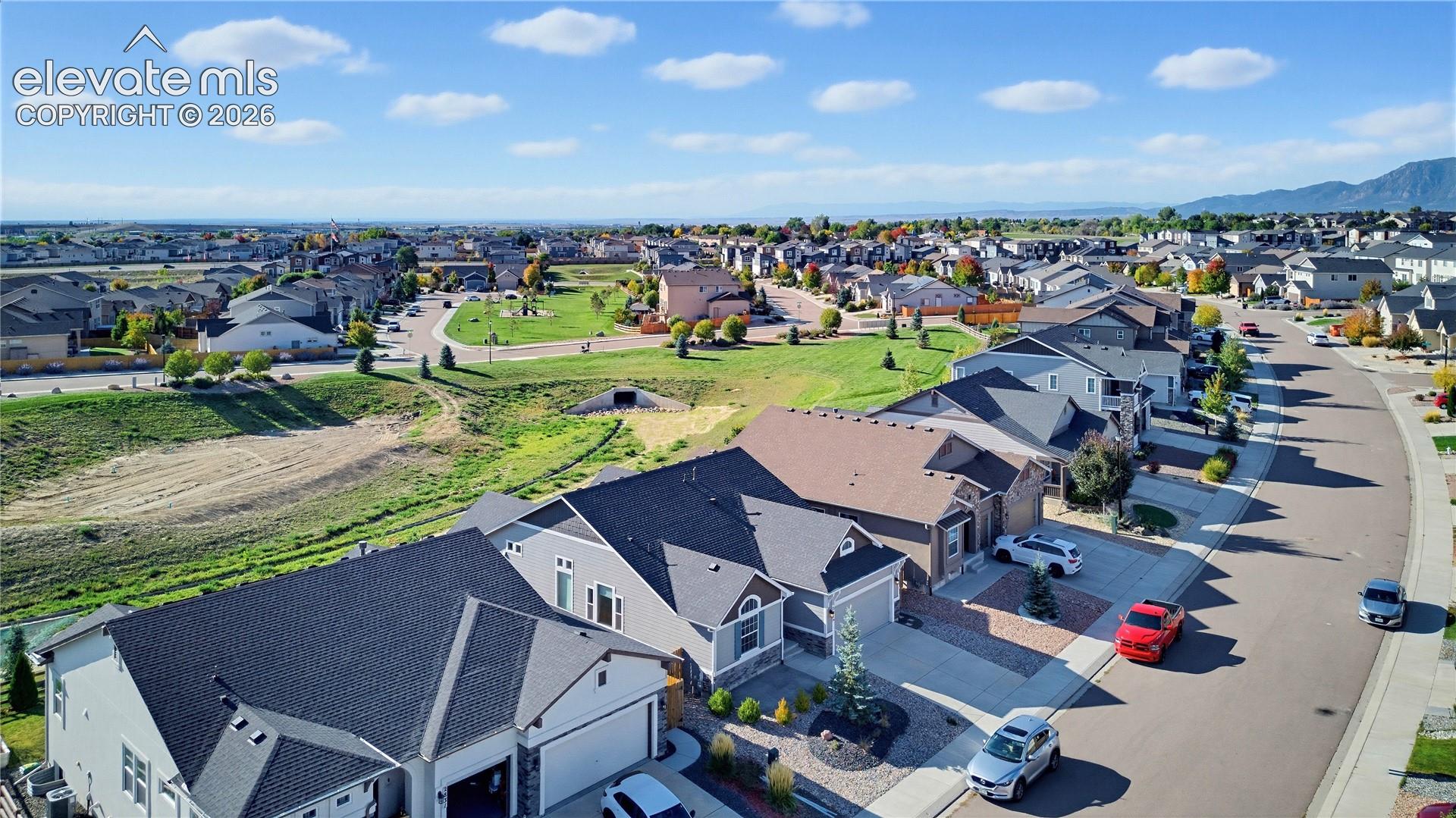 Aerial perspective of a suburban neighborhood featuring multi-level residential homes, asphalt streets, manicured green space, and a prominent mountain backdrop