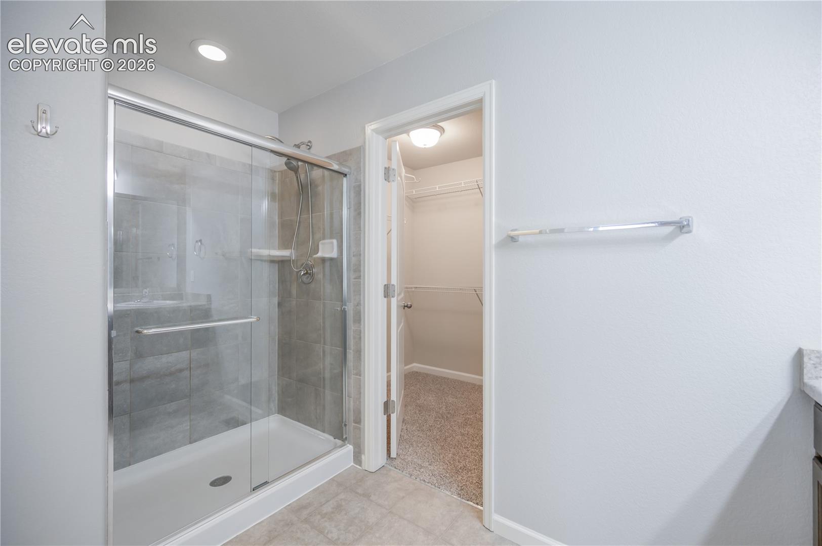 Walk-in shower with floor-to-ceiling tile surround and glass enclosure, integrated shelving, recessed lighting, and reach-in storage with built-in wire shelving