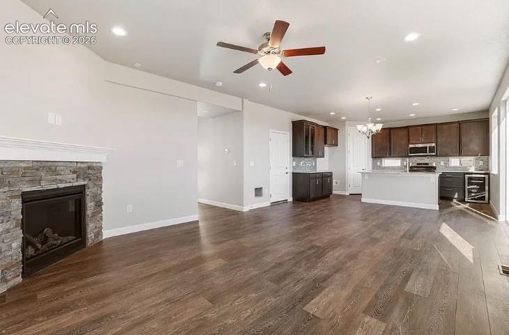 Open-concept interior featuring wood-finish flooring, stone-surround fireplace, recessed lighting, ceiling fan, and dark wood cabinetry with a built-in wine refrigerator