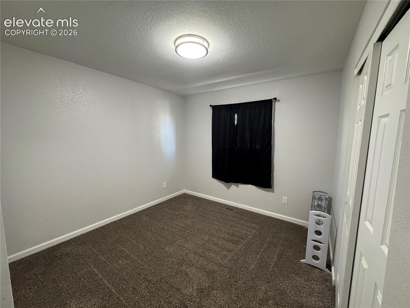 Neutral wall paint, textured ceiling, flush-mount ceiling light, dark-toned carpet, and sliding closet doors