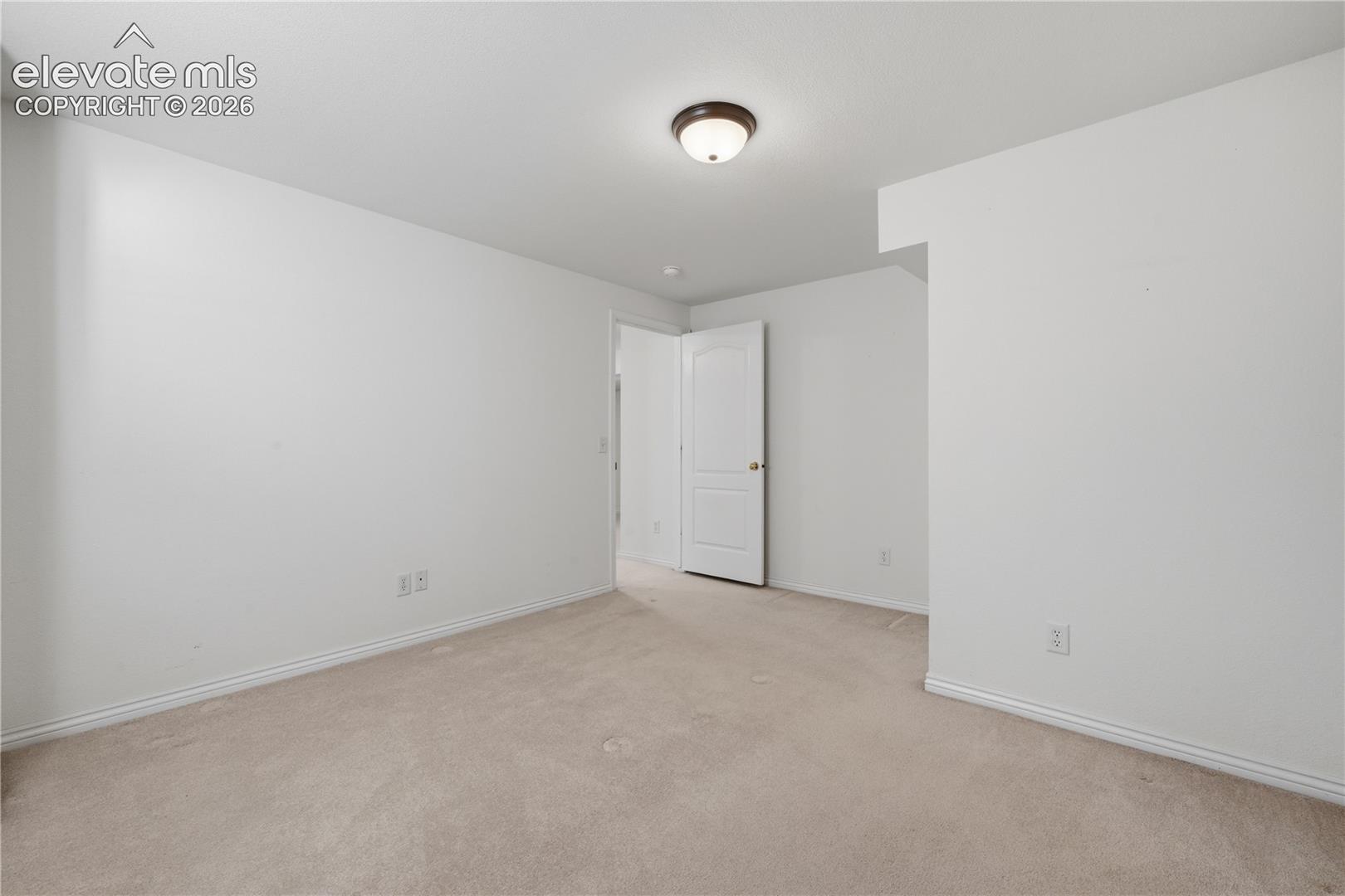 Neutral-toned wall-to-wall carpeting, crisp white walls, flush-mount ceiling lighting, and a solid-core interior door with a brushed-metal handle