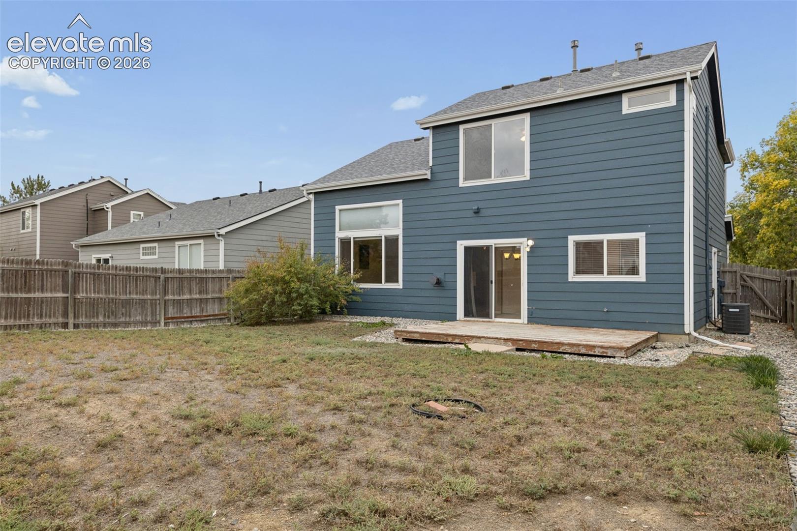 Two-story exterior featuring blue horizontal siding, a rear wood deck, multi-pane windows, and a fenced-in yard