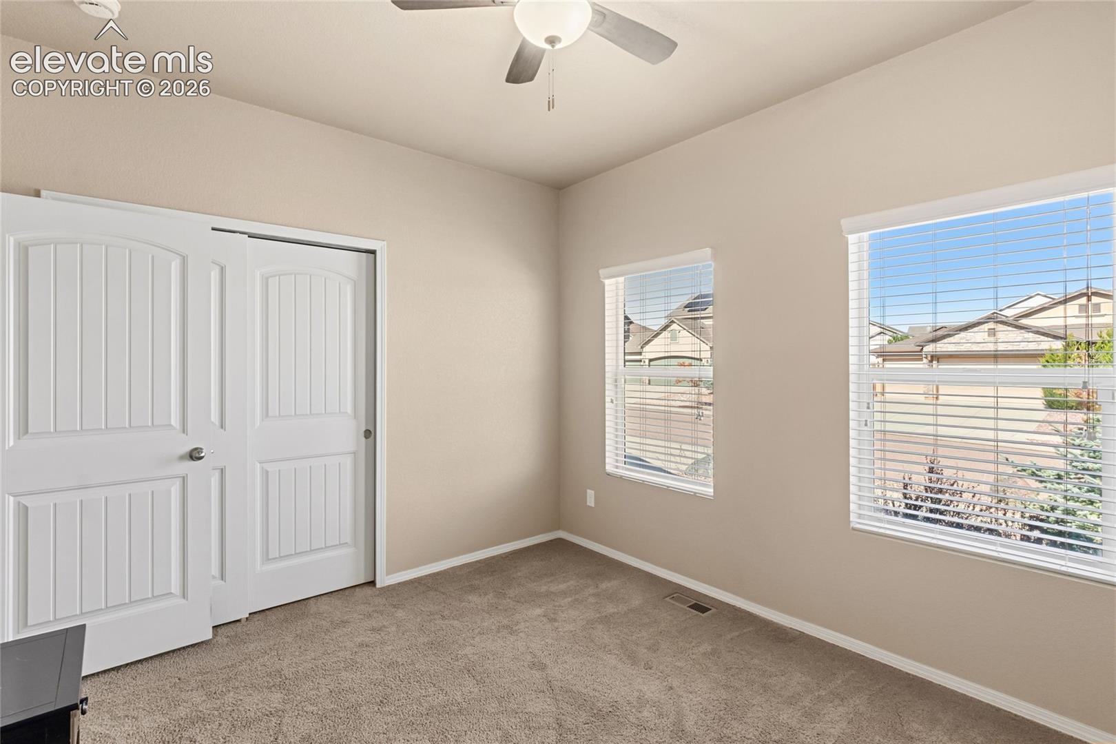 Neutral-toned room featuring plush wall-to-wall carpeting, two dual-pane windows with fitted horizontal blinds, and a white dual-panel sliding closet door