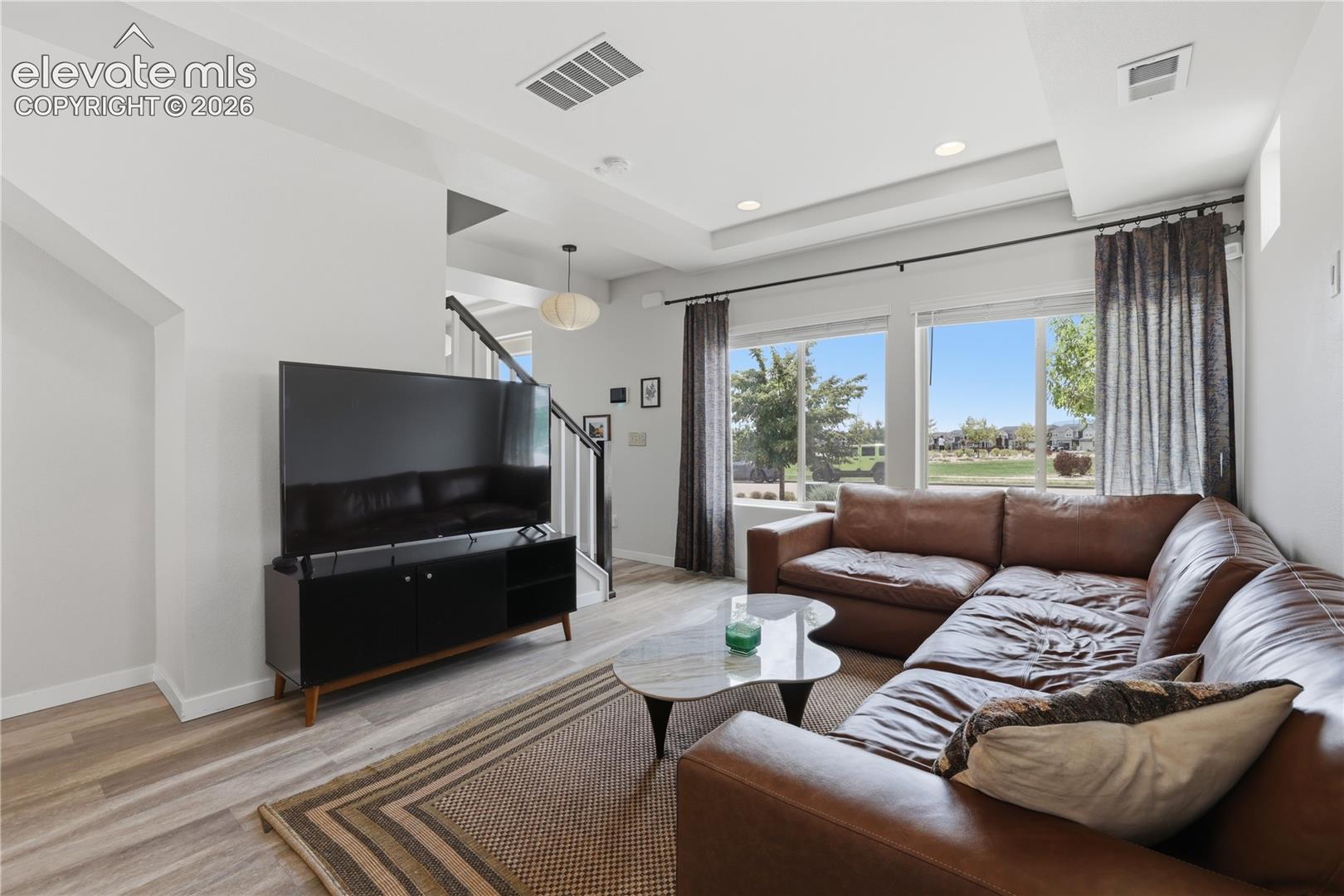 Spacious living area featuring large windows, wood-finish flooring, recessed lighting, and a tray ceiling