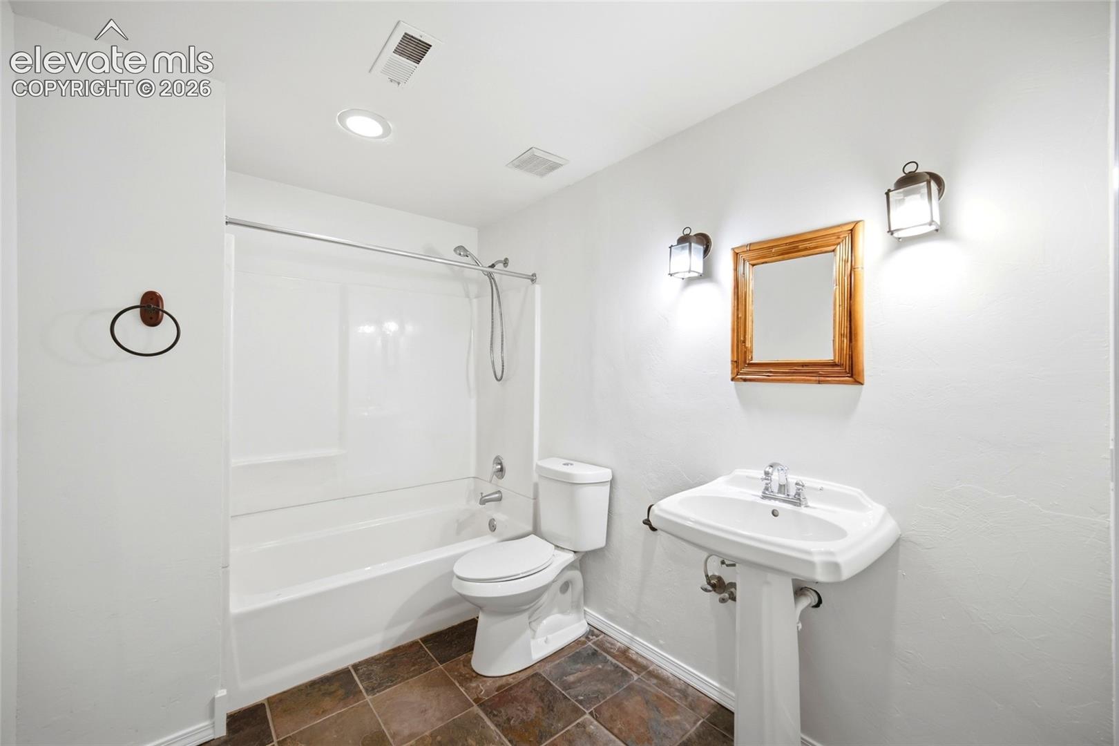 Bathroom featuring a white pedestal sink, a combined tub and shower unit, ceramic tile flooring, and dual wall-mounted light fixtures