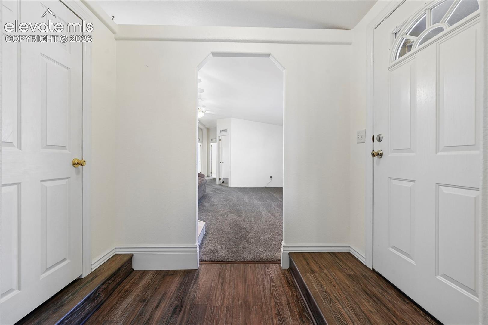 Entryway featuring wood-finish flooring, a white exterior door with an arched glass inset, and a geometric architectural archway