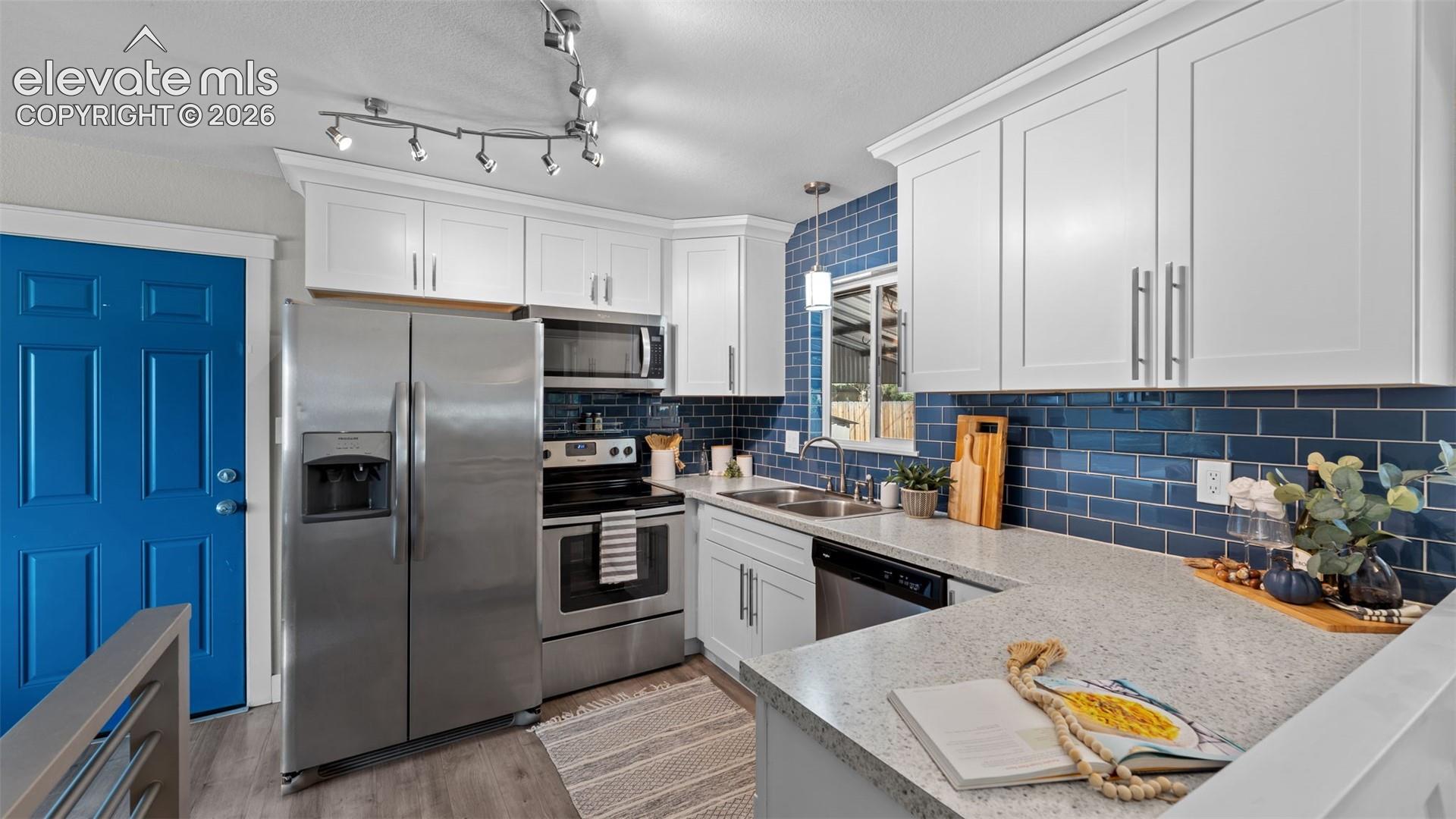 White shaker cabinetry, stainless steel appliances, blue subway tile backsplash, light wood-finish flooring, and light speckled countertops