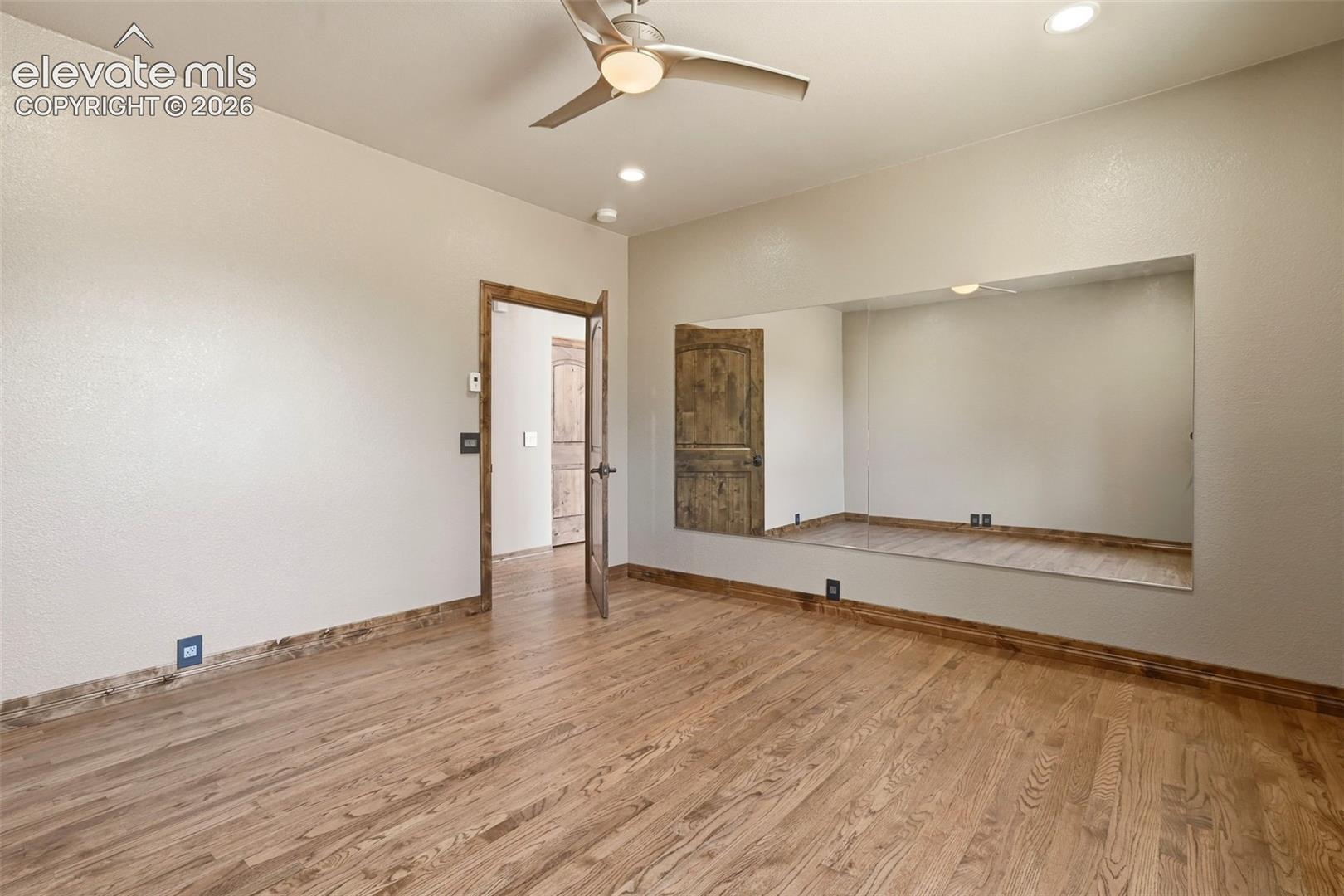Spacious room featuring wood-finish flooring, a built-in mirrored alcove, and a rustic wood door with coordinating trim