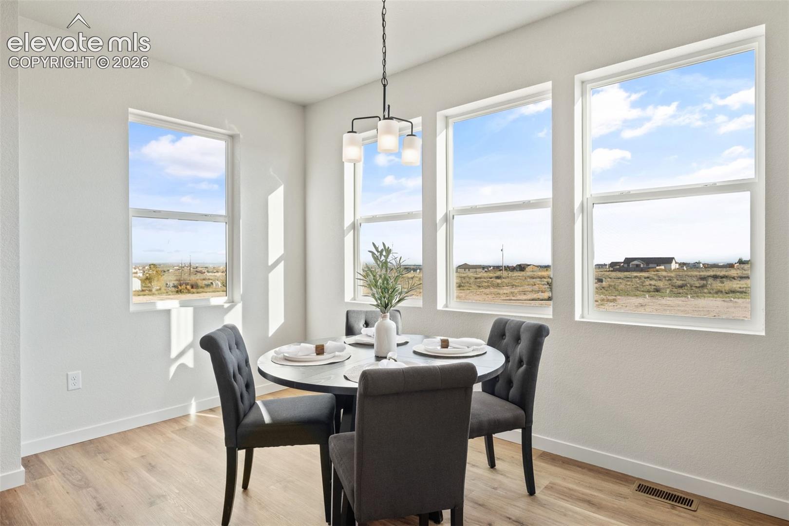 Open-concept dining area featuring multiple windows, wood-finish flooring, and a contemporary chandelier