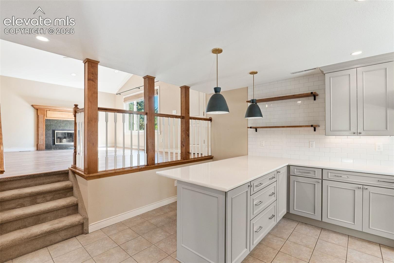 Kitchen featuring gray shaker-style cabinetry, white quartz countertops, subway tile backsplash, and two matte finish pendant lights, complemented by wood-post railings and tile flooring
