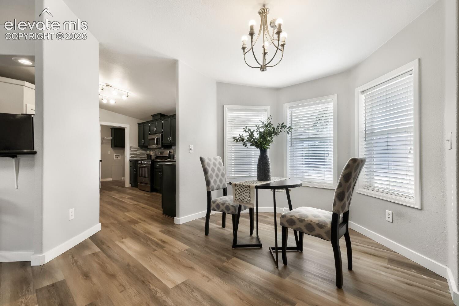 Bay area featuring three windows with horizontal blinds, wood-finish flooring, and a multi-arm chandelier