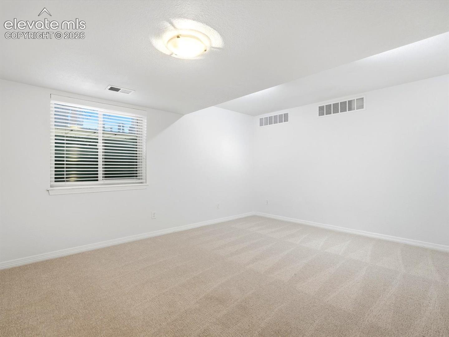 Neutral-toned wall-to-wall carpeting, crisp white walls, and a recessed ceiling light fixture, featuring a dual-pane sliding window with integrated blinds