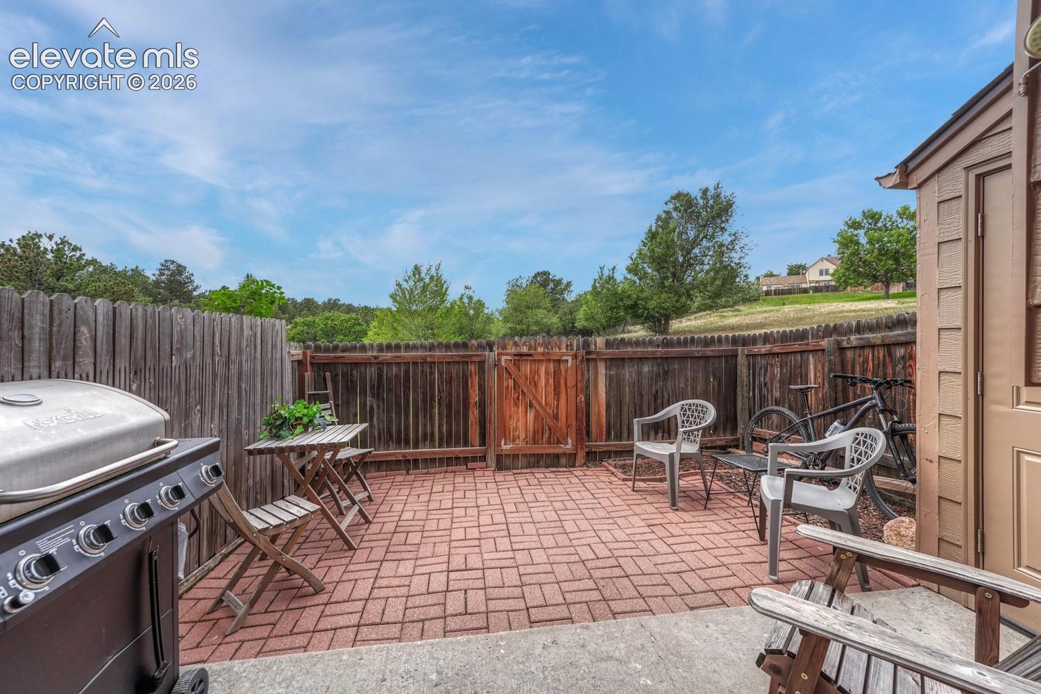 Fully fenced back patio features pavers and garden beds