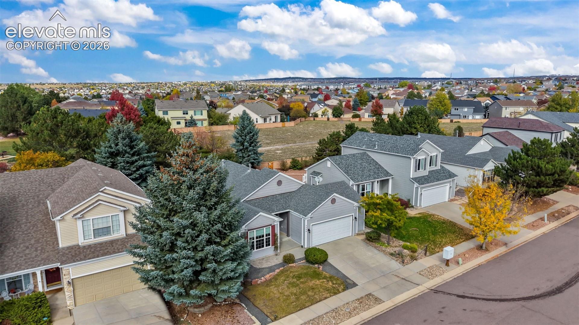 Aerial perspective of a multi-level suburban residence featuring light-toned exterior siding, a shingle roof, an attached garage, and landscaped front yard greenery