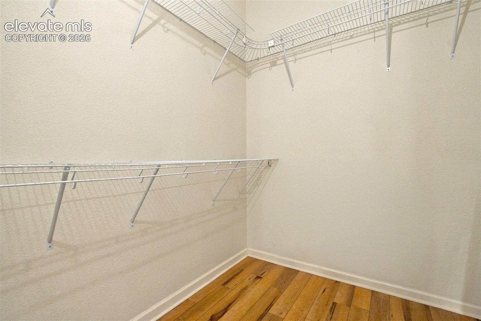 Primary walk-in closet featuring wood-finish flooring and multi-level white wire shelving