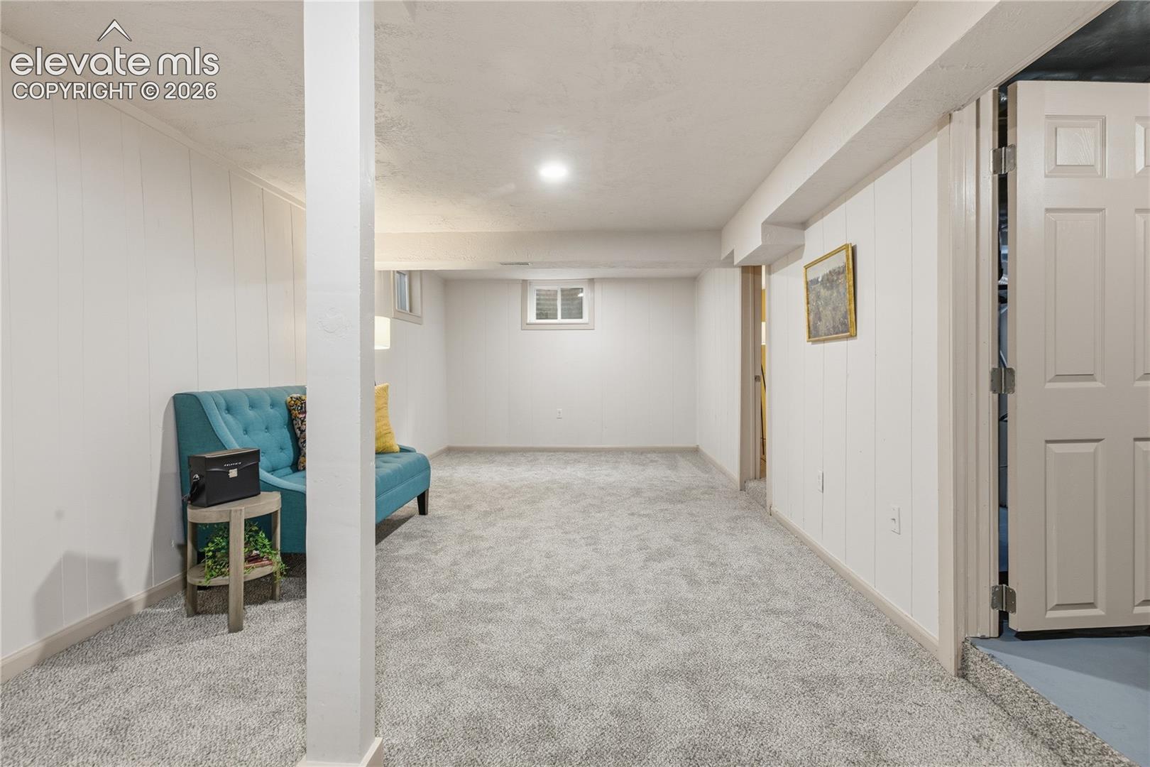 Open-concept interior featuring vertical paneling, neutral wall-to-wall carpeting, recessed ceiling lighting, and a six-panel interior door