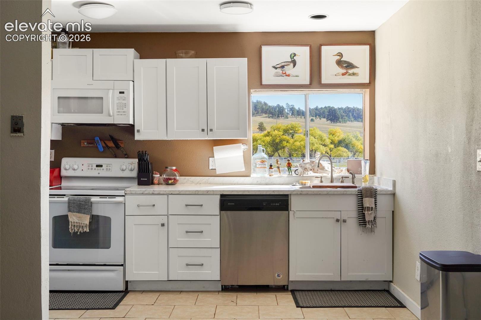 Kitchen featuring white cabinetry, light-toned countertops, a stainless steel dishwasher, a white oven, and an over-the-range microwave