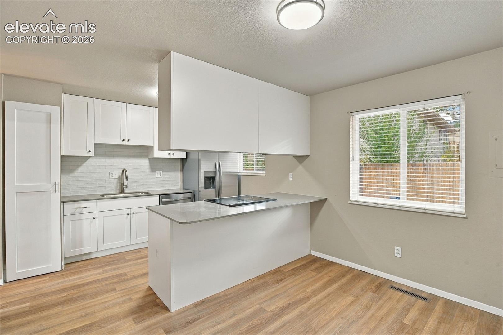 Kitchen featuring white cabinetry, solid-surface countertops, a tile backsplash, stainless steel sink, and wood-finish flooring