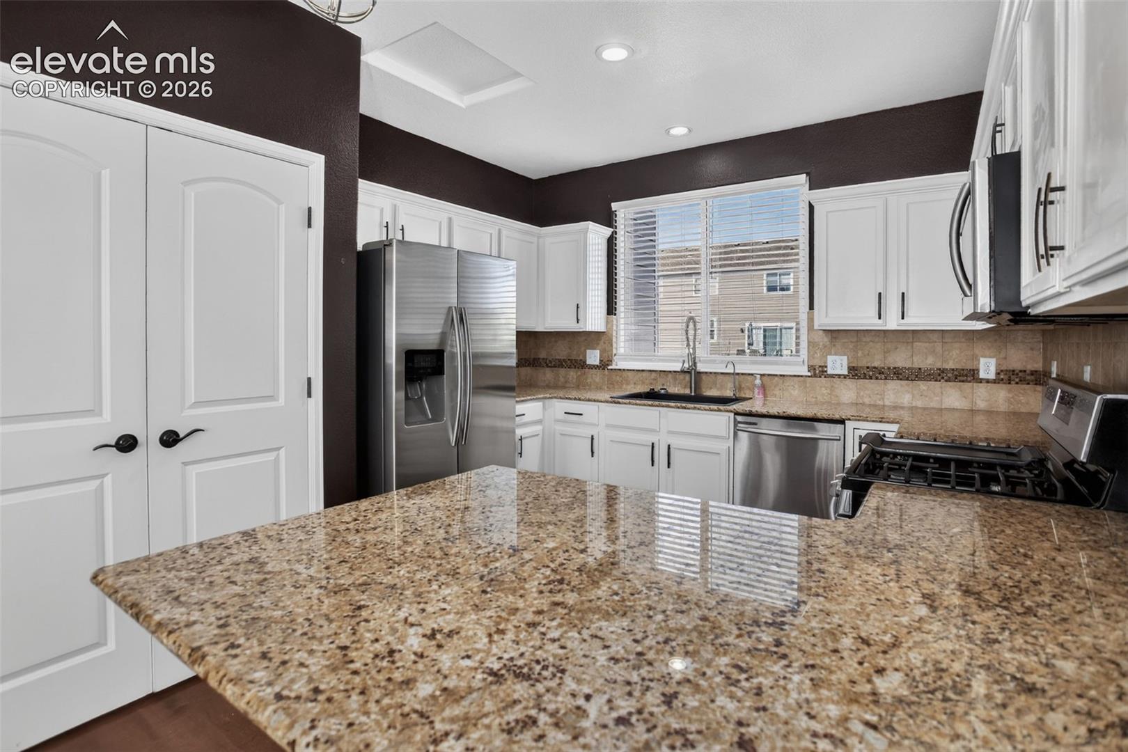 Kitchen featuring white cabinetry, stainless steel appliances, speckled countertops, a tiled backsplash, and dual white paneled doors