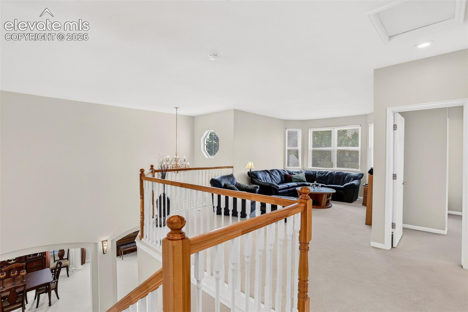 Open landing with wood and white baluster railing, showcasing a chandelier, recessed lighting, and large windows