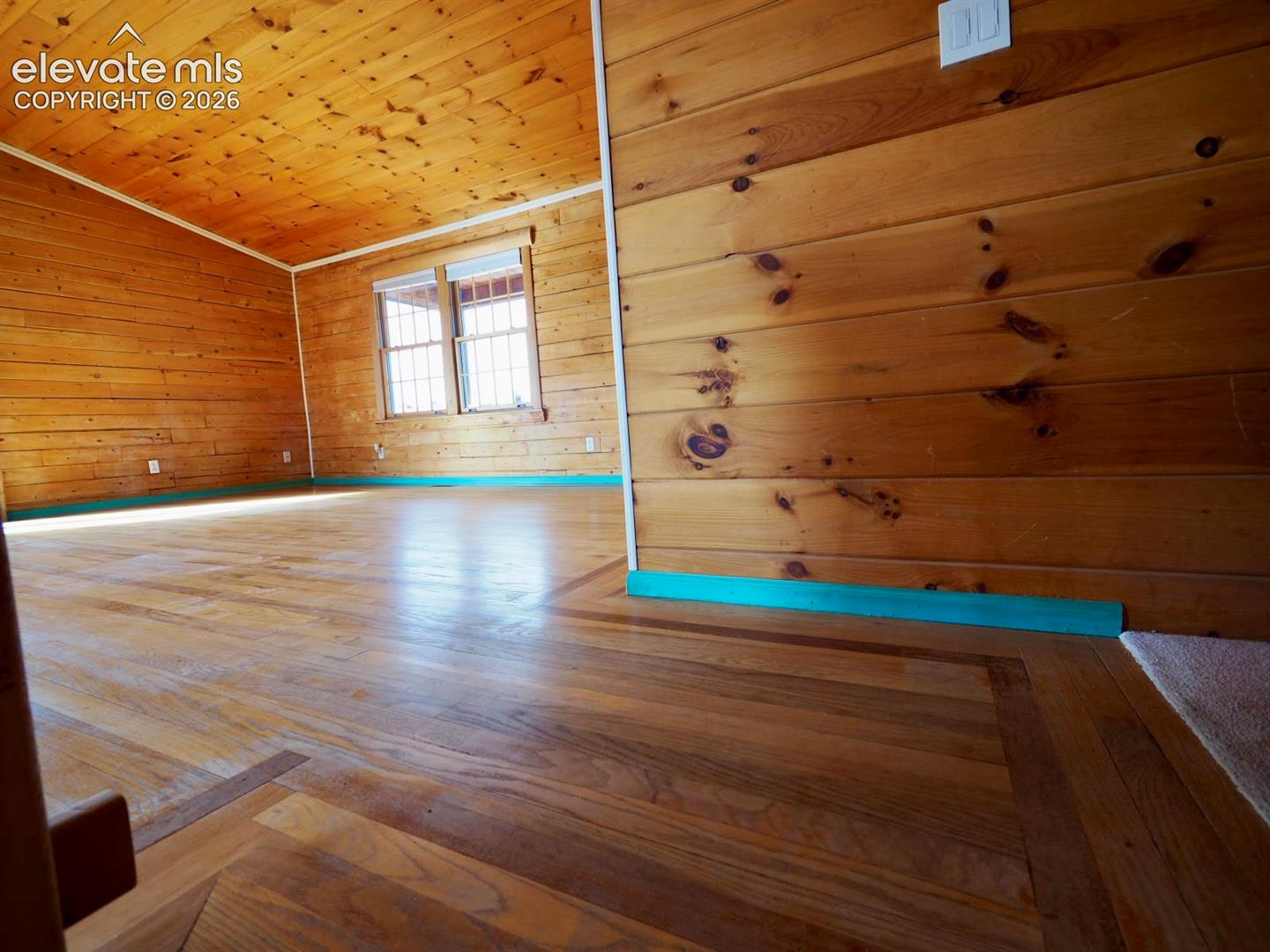 Interior space featuring knotty wood-paneled walls and ceiling, wood-finish flooring with inlay detailing, and dual-pane windows