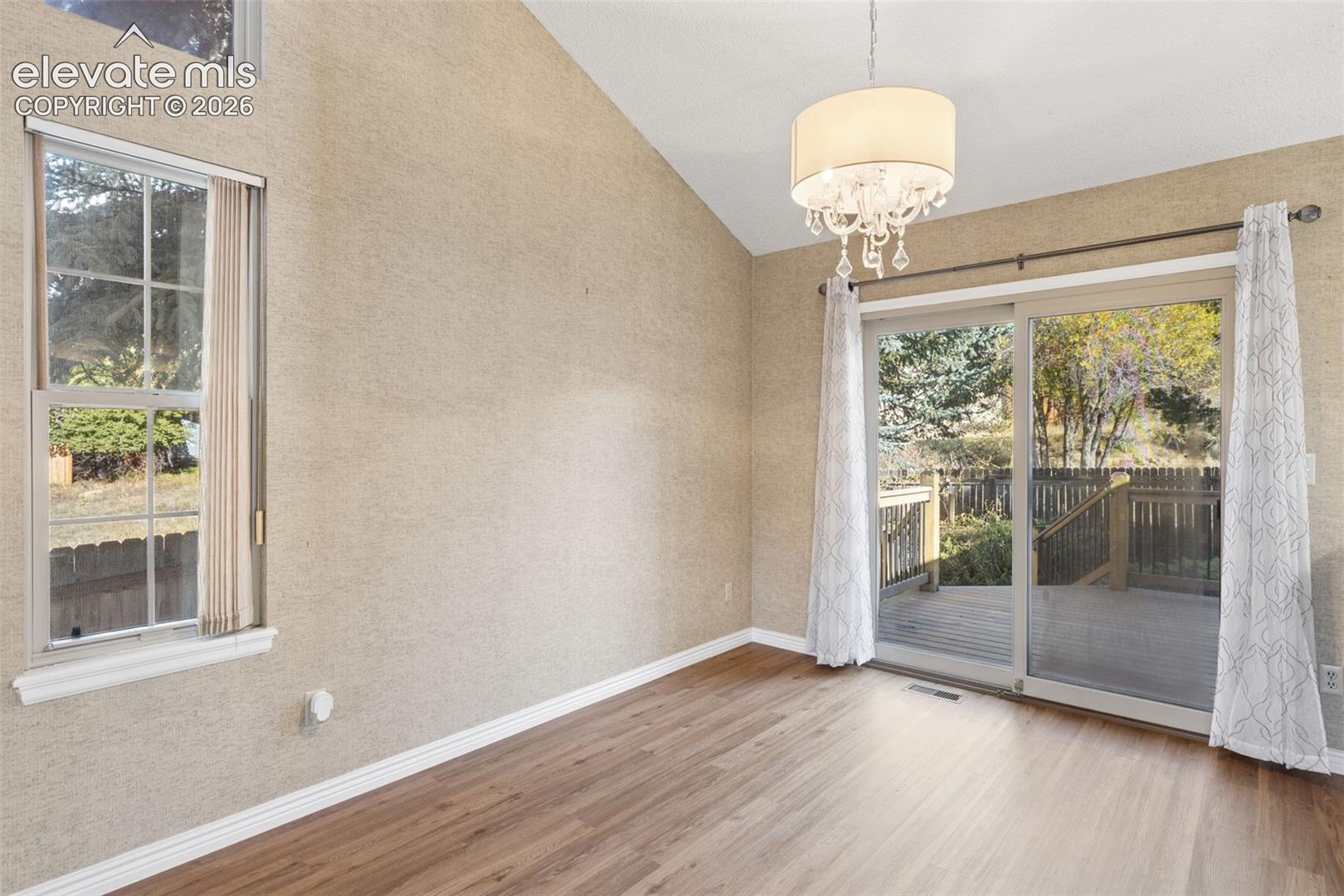 Vaulted ceilings, wood-finish flooring, sliding glass door, tiered chandelier, and picture window with natural light