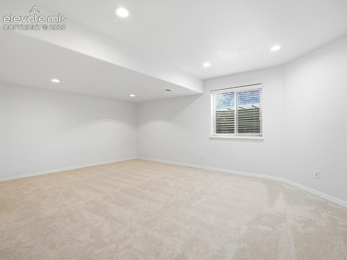 Neutral interior space featuring wall-to-wall carpeting, recessed ceiling lighting, and a single window with horizontal blinds