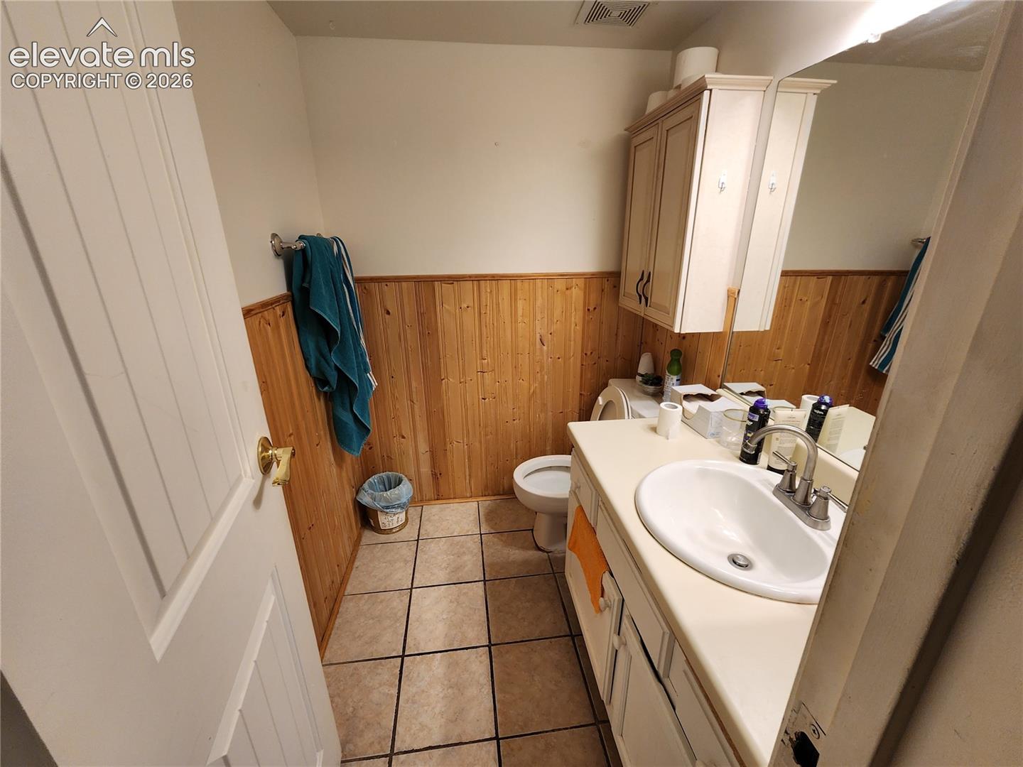 Bathroom featuring tile flooring, wood-panel wainscoting, a vanity with a surface-mounted sink, and a wall-mounted medicine cabinet