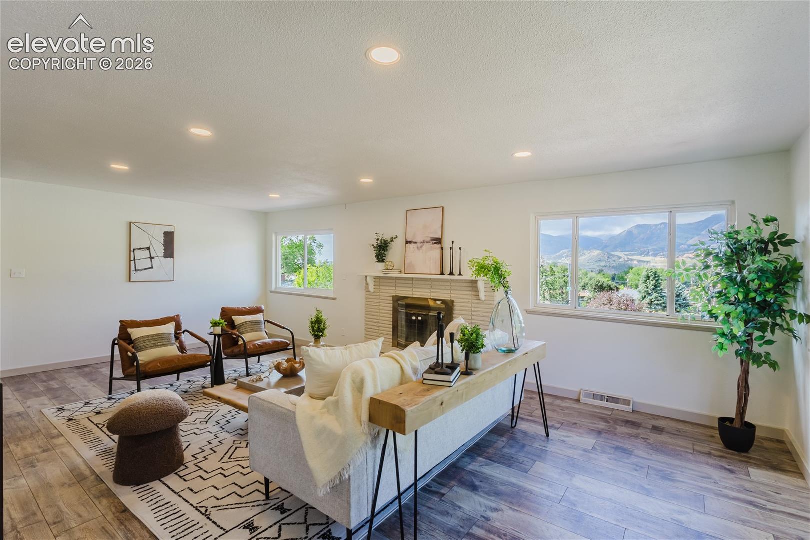 Bright living space featuring wood-finish flooring, a contemporary fireplace with a tile surround, and expansive windows showcasing mountain scenery
