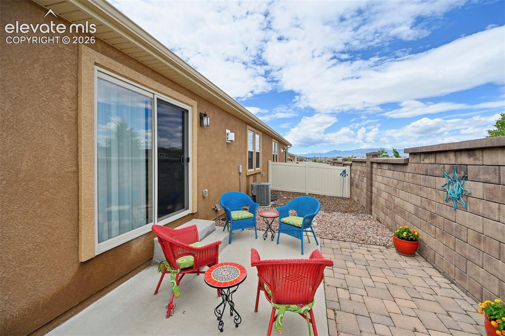 Paved patio area featuring a block retaining wall, a sliding glass door, and stucco exterior siding