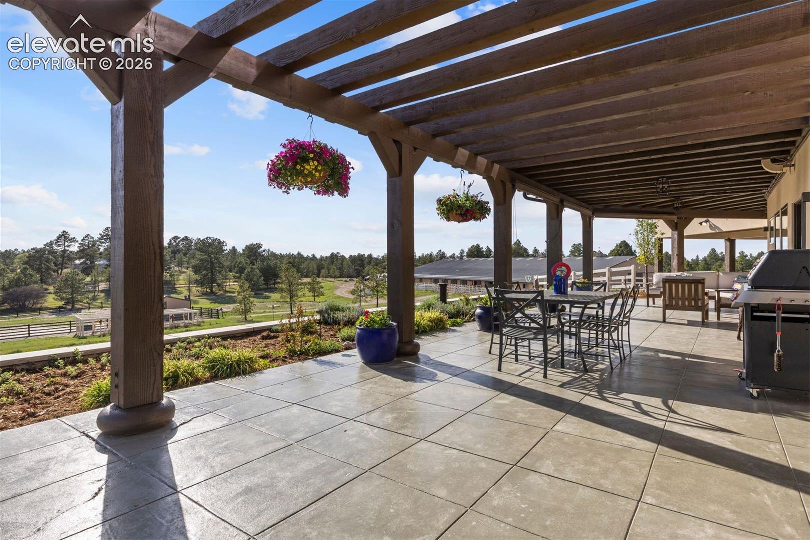 Expansive patio, partially covered by two striking pergolas, wraps the full perimeter of the home, seamlessly connecting indoor and outdoor living with multiple entertaining areas.
