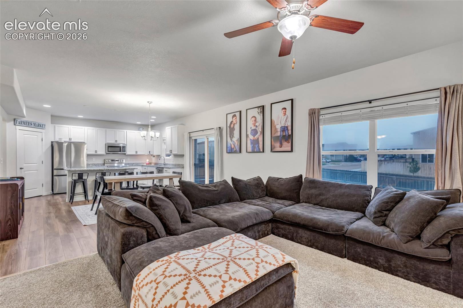 Open-concept living and kitchen area featuring a sectional seating arrangement, wood-finish flooring throughout, recessed ceiling lighting, ceiling fan, and expansive windows with panoramic water and landscape vistas