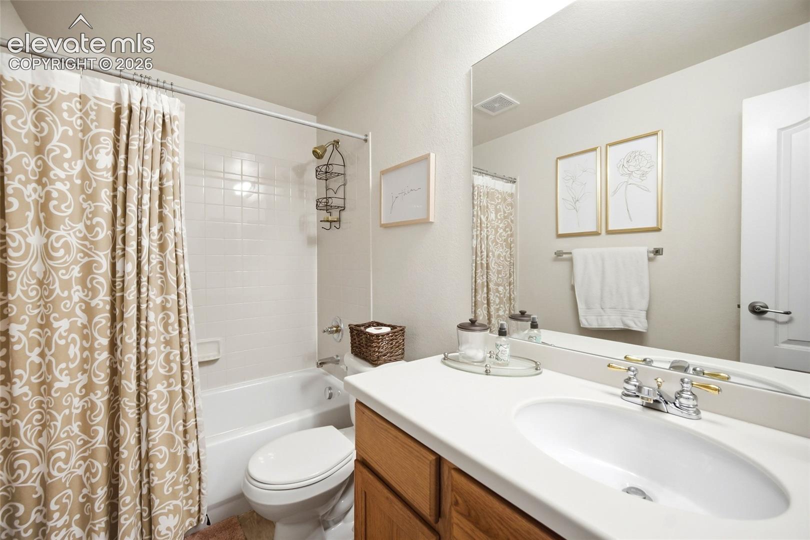 White bathtub with a tiled shower surround, wood-finish vanity with a white countertop, and an integrated rectangular sink