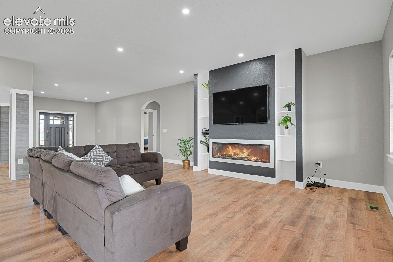 Recessed lighting illuminates the wood-finish flooring and a built-in media wall featuring an electric fireplace and integrated shelving