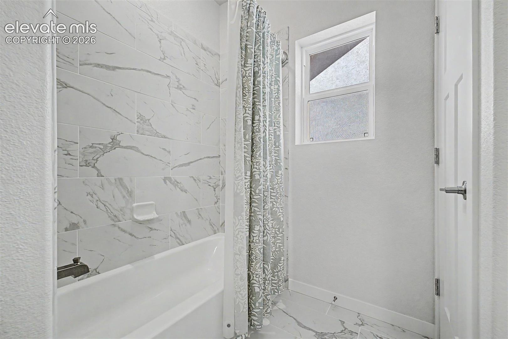 The tub and shower combo is finished in dramatic marble-look tile, with a decorative curtain and frosted window letting in light without sacrificing privacy — practical luxury for every member of the household.
