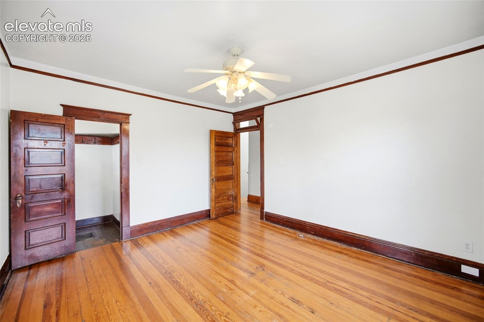 Interior space featuring wood-finish flooring, stained wood trim, five-panel wood doors, and a ceiling-mounted light fixture with a fan