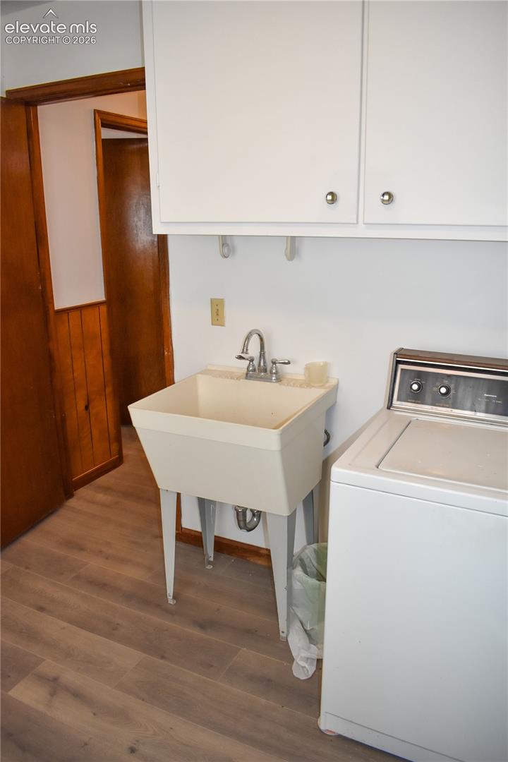 Wood-finish flooring, white wall-mounted cabinetry, utility sink with chrome faucet, and wood-paneled wall accent