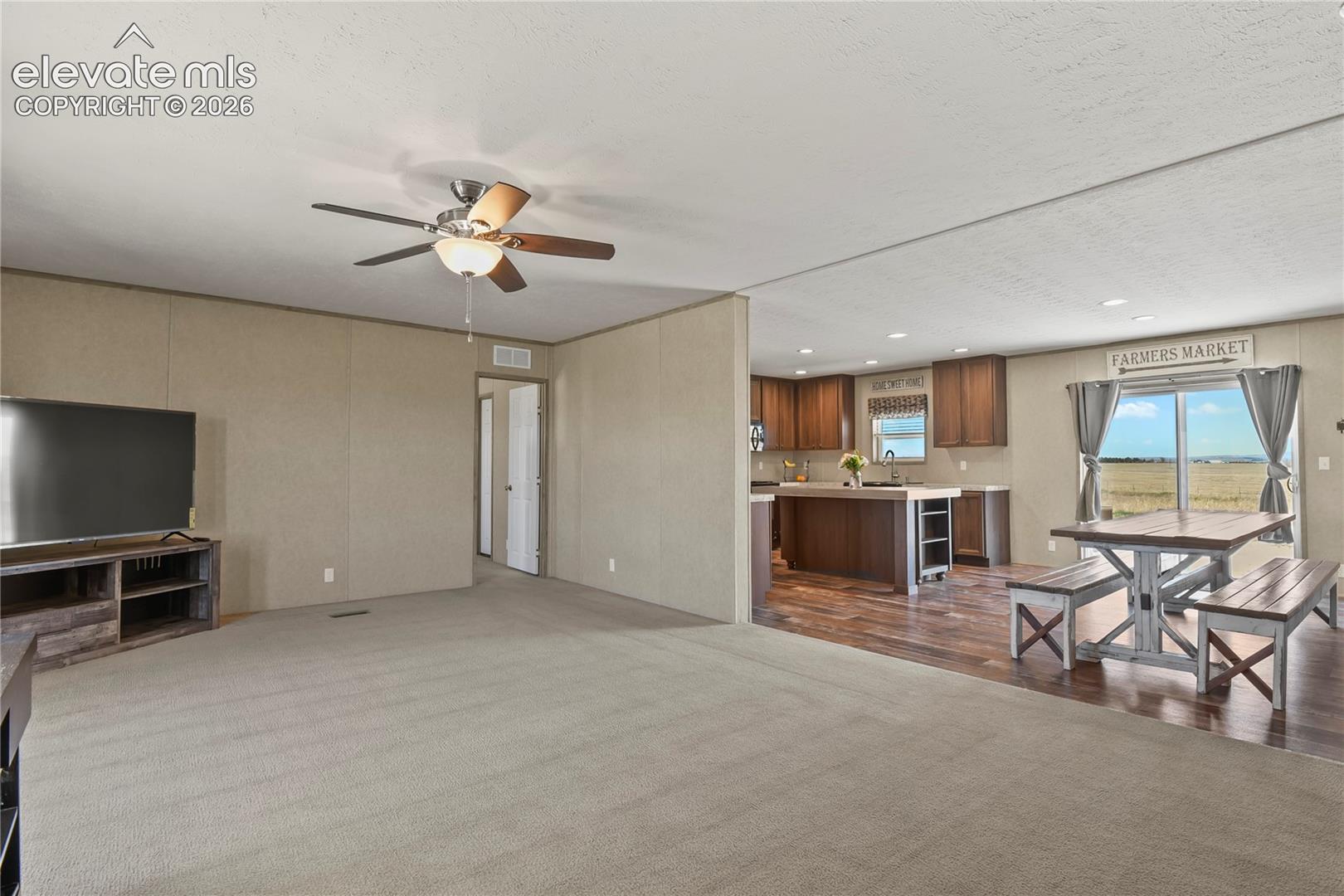Neutral-toned wall panels, carpeted flooring, wood-finish cabinetry, kitchen island with countertop, and sliding glass doors