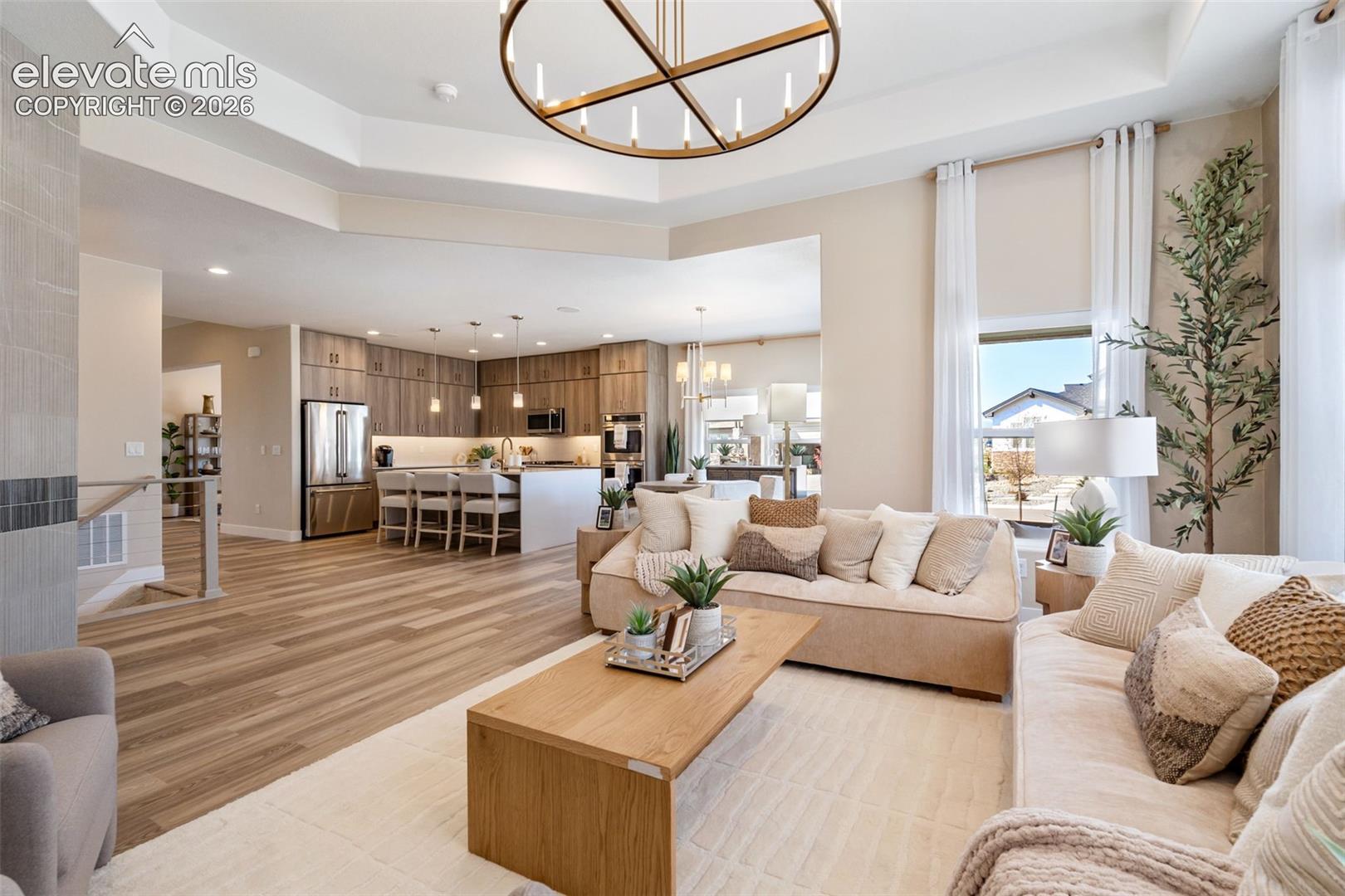 Open-concept interior featuring wood-finish flooring, tray ceilings, a modern circular chandelier, and a kitchen equipped with a center island and built-in stainless steel appliances