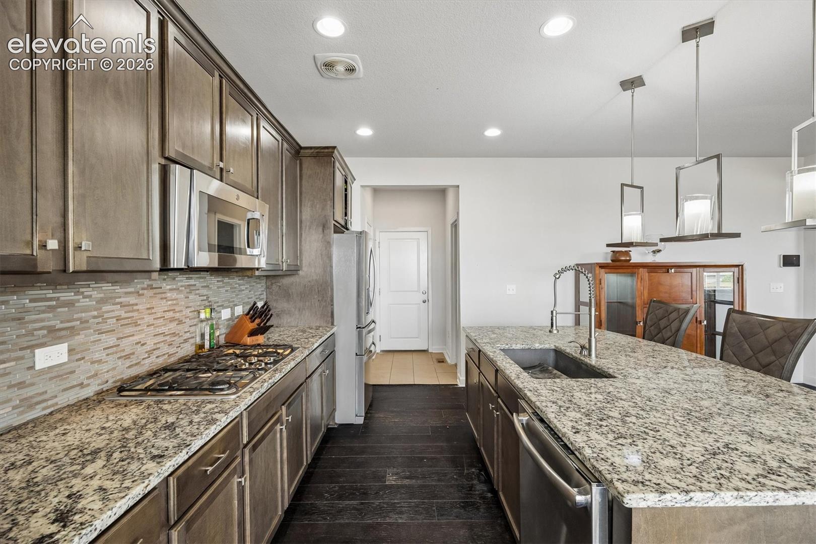Modern kitchen featuring dark wood-finish flooring, light-colored stone countertops, and stainless steel appliances
